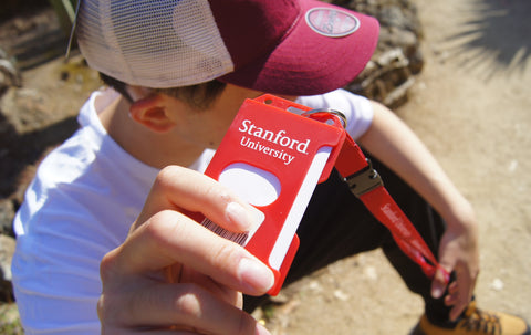 Student holding a red ID holder with white letters reading "Stanford University"
